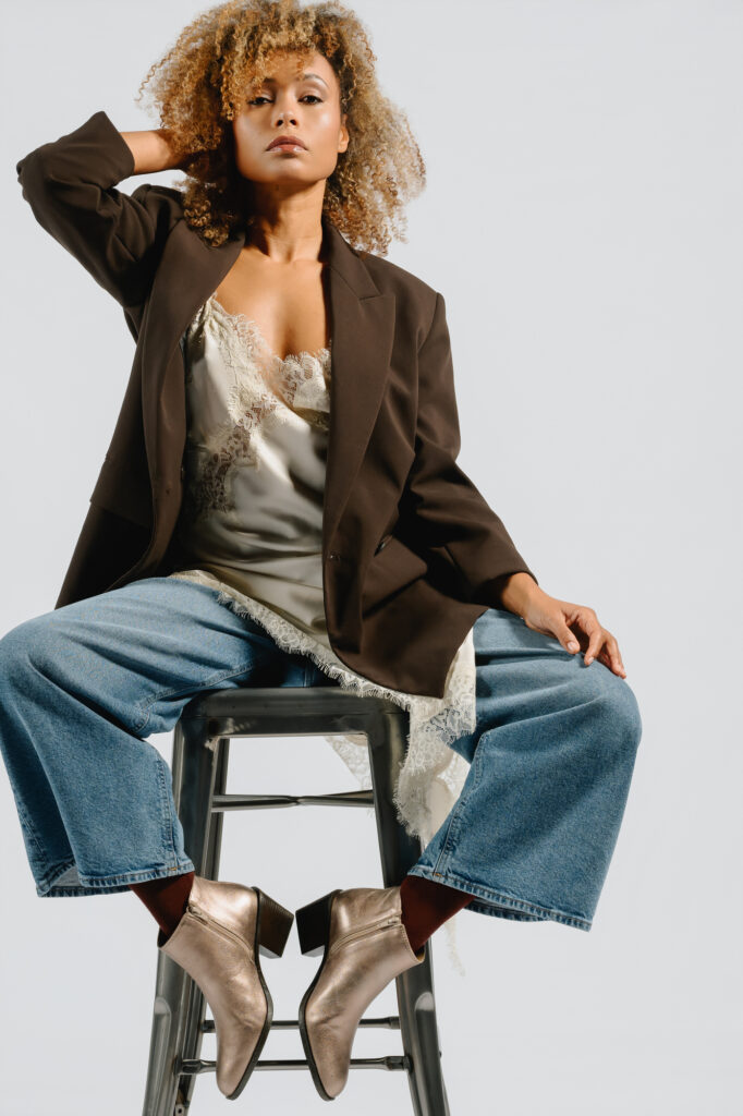 Close-up of AQA rosegold metallic ankle boots worn by a model standing near a water feature on a city street - Spring/Summer 2026 Collection.